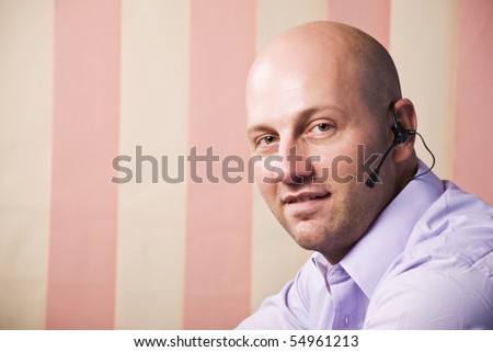 Portrait of nice customer service bald man with headset looking at you,copy space for text message in left part of image,vertical blinds background