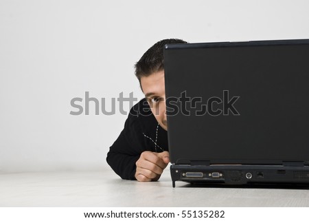 Man looking  hiding behind laptop and lying on wooden floor,copy space for text message in left part of image