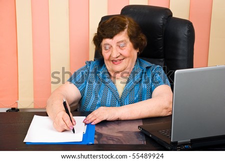 Laughing elder woman write on paper and sitting at desk in office