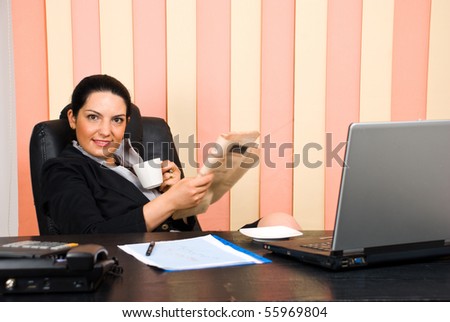 Manager woman  sitting in her chair at desktop ,holding a cup of coffee and a newspaper and smiling