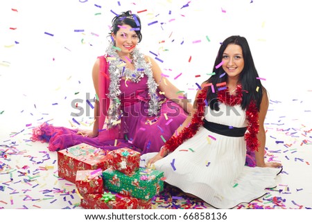 Beautiful women in elegant dresses sitting both on floor with Christmas presents while many confetti falling down over them