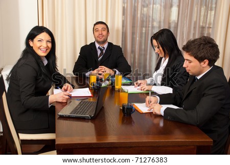 Two business people laughing and other two business people being serious and writing at business meeting