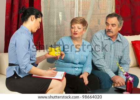 Real estate agent presenting a minaiture house to mature couple in their house