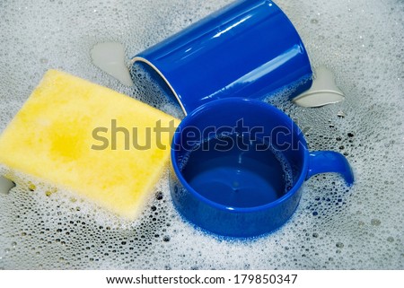 Two blue Coffee Cups with  yellow Sponge in a Kitchen Sink, close up / Washing Dishes
