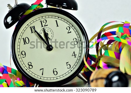 close up of  a black retro alarm clock, around midnight, with paper streamers and cork from a bottle of sparkling wine,  horizontal, slanted / New YearÂ´s Eve
