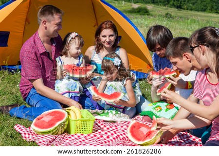 outdoor group portrait of happy company having picnic near the tent in park and enjoying watermelon