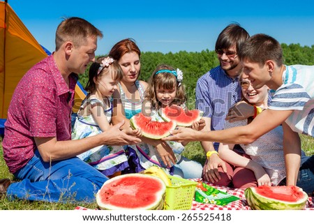 outdoor group portrait of happy family having picnic on green grass in park and enjoying watermelon