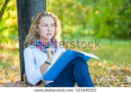 Thoughtful girl student sits and writes in the autumn park