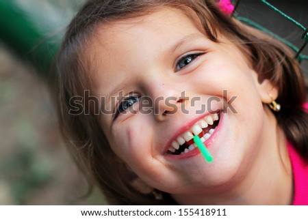 A lollipop sticks out from the laughing girl\'s mouth.