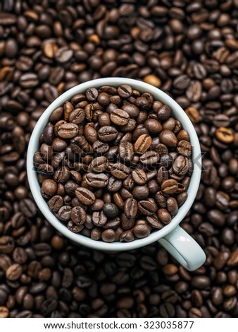 Cup full of roasted coffee beans with a lot of coffee on background