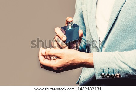 Man in formal suit, bottle of perfume, closeup. Fragrance smell. Men perfumes. Fashion cologne bottle. Man holding up bottle of perfume. Men perfume in the hand on suit background. Copy space.
