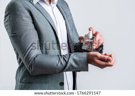 Man holding up bottle of perfume. Men perfume in the hand on suit background. Man in formal suit, bottle of perfume, closeup. Fragrance smell. Men perfumes. Fashion cologne bottle.