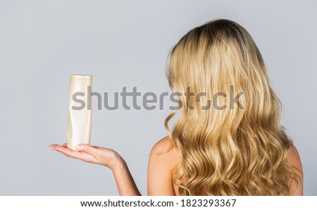 Woman hold bottle shampoo and conditioner. Woman holding shampoo bottle. Beautiful blonde girl with a bottle of shampoos in hands. Girl with shiny and long hair. Woman long hair.
