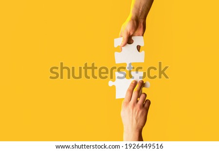 Closeup hands of man connecting jigsaw puzzle. Two hands trying to connect couple puzzle with yellow background. Hand connecting jigsaw puzzle. Man hands connecting couple puzzle piece.