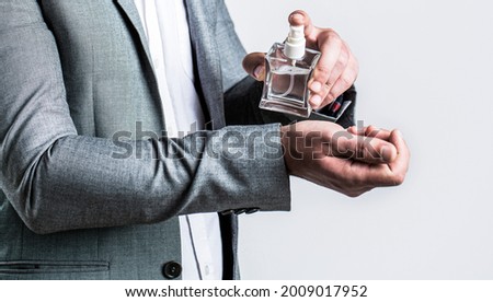 Fragrance smell. Men perfumes. Fashion cologne bottle. Man holding up bottle of perfume. Men perfume in the hand on suit background. Man in formal suit, bottle of perfume, closeup.