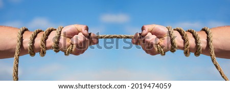 Two hands, helping hand, arm, friendship. Rope, cord. Hand holding a rope, climbing rope, strength and determination. Rescue, help, helping gesture or hands. Conflict tug of war