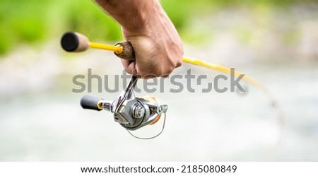 Fishings reel close-up on the background of the river. Fisherman hand holding fishing rod with reel. Fishing Reel. Fishing Rod with Aluminum Body Spool. Imagine de stoc © 