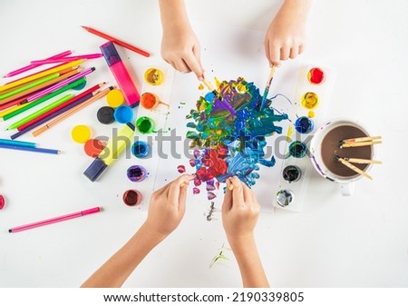 Hands paint brush. Kid hands painting at the table with art supplies. Hands with brush painting with watercolor abstract stains. Drawing on a white sheet of paper. Creativity and art.