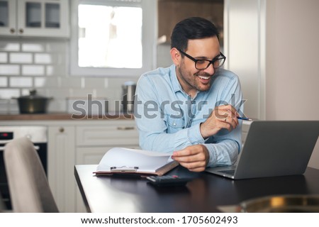 Young man working from home doing paperwork while using laptop and holding pen in his hand. Foto stock © 