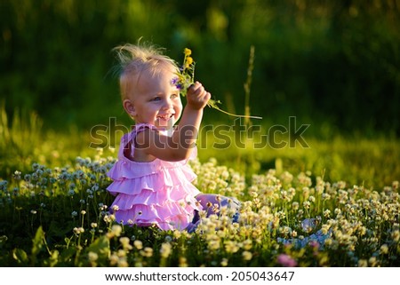 A cute little smiling girl playing with clover flowers in the meadow  in a sunny summer day