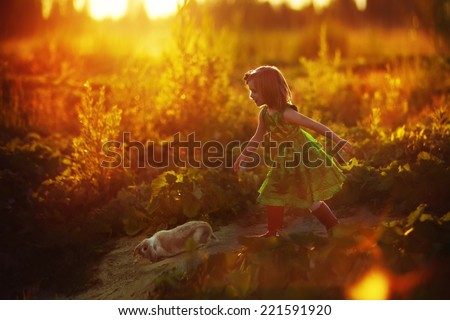 A little pretty girl in a green dress running after the rabbit on a sunny summer evening. Kids are playing