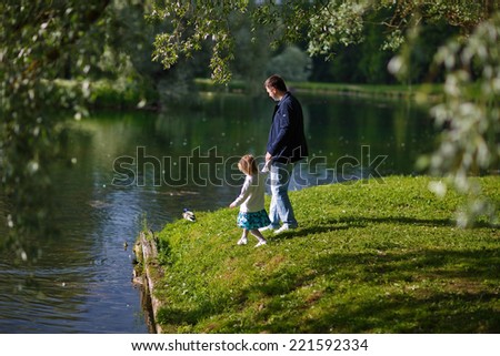 Back view of a father and his little daughter walking along the river shore