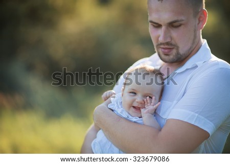 Happy family: young strong healthy father in white clothes walking with his new-born daughter in the park on a sunny summer day.