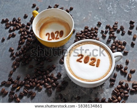 Goodbye 2020, Hello 2021 holidays food art theme coffee cups with number 2021 and 2020 on frothy surface flat lay on grey cement background with coffee beans. Holidays food art for Happy New Year.