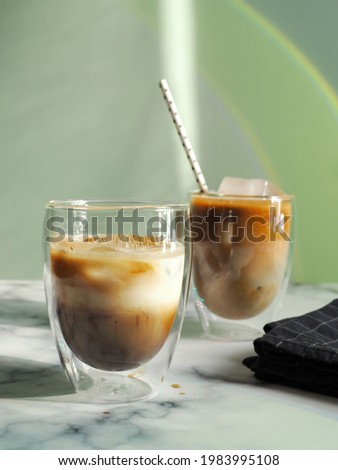 Iced caramel latte coffee in double wall insulated glasses with fancy eco friendly paper straw on white marble background and green wall with rainbow light reflection. Refreshing, enjoy summer drinks. 商業照片 © 