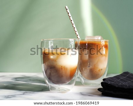 Iced caramel latte coffee in double wall insulated glasses with fancy eco friendly paper straw on white marble background and green wall with rainbow light reflection. Refreshing, enjoy summer drinks. 商業照片 © 