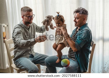Male gay couple with adopted baby girl at home - Two handsome fathers playing with their daughter - Lgbtq+ family at home - Diversity concept and LGBTQ family relationship