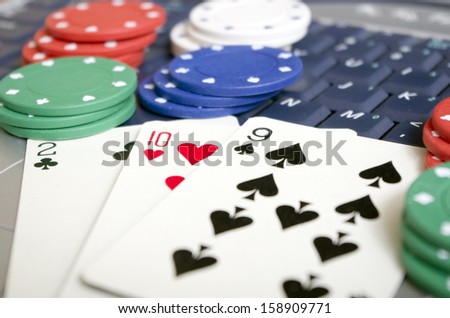 Online Gambling Hand of playing cards laid on computer keyboard with a selection of betting chips. this depicts the modern trend of gambling and playing cards online with competitors world wide.