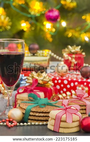 Christmas Gifts, Biscuit Cookies and Red Wine Christmas biscuits tied with ribbons, a glass of Red Wine, with presents in front of a Christmas tree, lit with a candle and Christmas tree lights