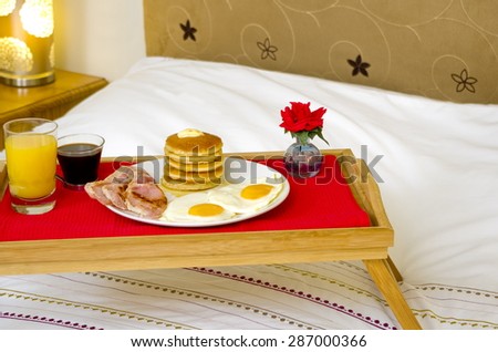 Pancake Breakfast Served in Bed\
A  tray with a Pancake Maple Syrup, bacon and egg breakfast on a double bed.