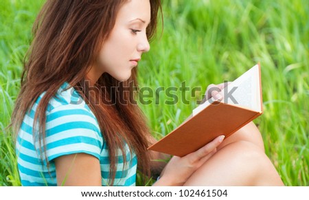 Portrait of beautiful young woman sits on grass and reading book at summer green park