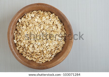 Rolled oats in a wooden bowl on a gray cloth.