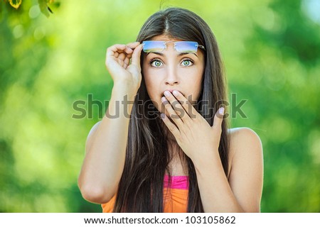 Portrait of young beautiful woman picks up glasses and closes his hand in surprise mouth, on green background summer nature.
