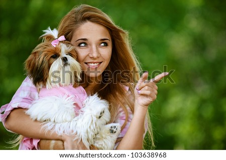 Portrait of beautiful smiling young woman with small dog, against green of summer park.