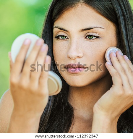 Portrait of young beautiful woman with bare shoulders causes powder to face, on green background summer nature.