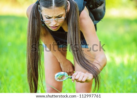 Portrait of young beautiful woman wearing backpack and looking bugs through magnifying glass, on green background summer nature.