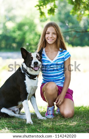Beautiful smiling teenage girl in blue blouse and black dog, against green of summer park.