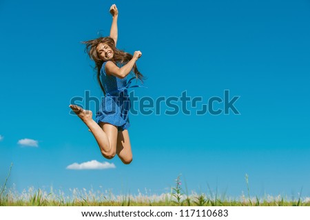 Beautiful dark-haired happy young woman jumping high in air, against background of summer blue sky.