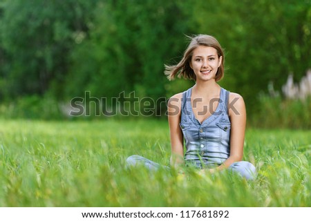 Beautiful laughing young woman sitting on grass, against background of summer green park.