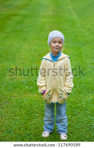 Beautiful little girl in yellow blouse and jeans standing on green lawn sheared.