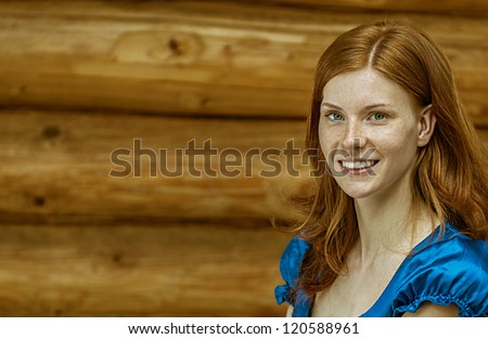 Portrait of dark-haired beautiful young woman in blue blouse, against background of log hut