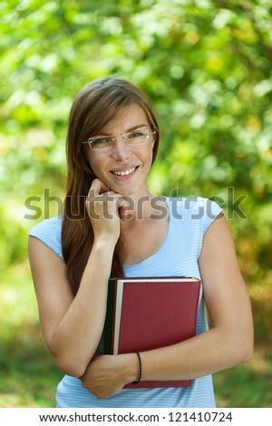 Portrait of beautiful young woman with books, against green of summer park.