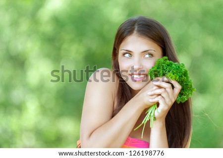 Portrait of beautiful smiling young woman with bunch of parsley, against summer green park.