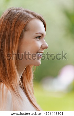 Portrait in profile of beautiful smiling young woman, against background of summer green park.