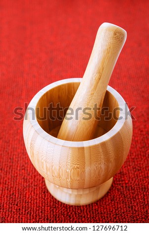 Large wooden mortar and pestle on red background.