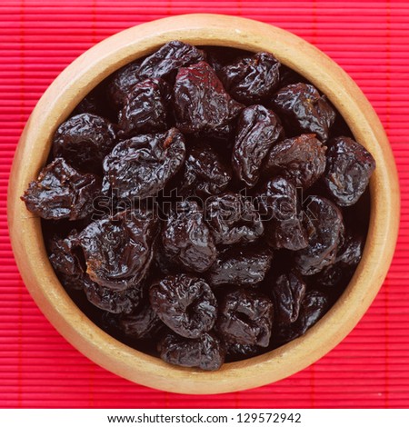 Dried prunes in wooden bowl on red bamboo table cloth.